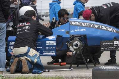 The U of T Racing Team’s pit crew kneel around their car, working hard on a wheel change and other fixes.