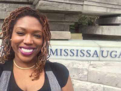 Desiree Kaunda-Wint smiles in front of the U of T Mississauga sign.
