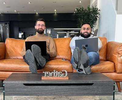 Mikael Castaldo and Osama Siddique sitting together on a couch with laptops and their feet up on a coffee table
