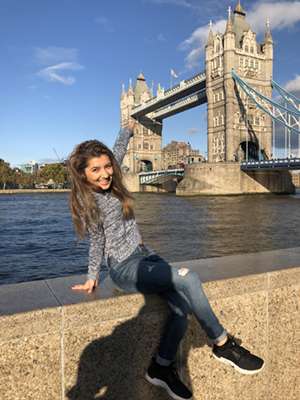 Zarina Mamadbekova sits on a riverside wall and points over the water at Tower Bridge, in London, U.K.