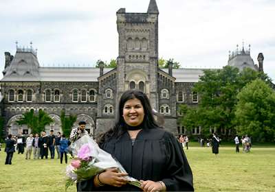 Aashni Shah smiles as she poses on Front Campus in her graduation robes and carrying flowers.