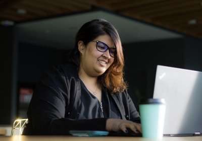 Aashni Shah smiles as she types onn a laptop.
