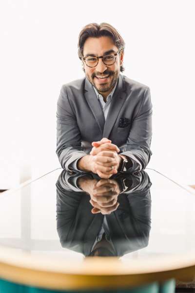 Adam Rodricks: a young white man laughing as he leans forward with hands folded on a table.