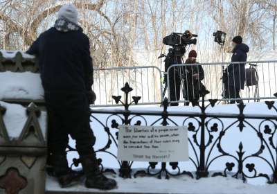 A woman approaches Annie Bergeron-Oliver, who is standing by a camera and light, outdoors on a snowy day.