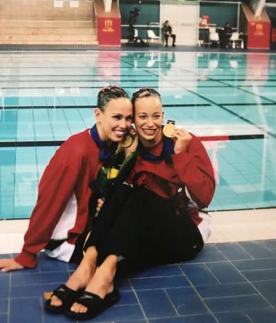Claire Carver-Dias and Fanny Letourneau sit, hugging, on the deck of a swimming pool and hold up their gold medals.