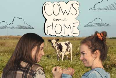 Two women making a pinky swear in front of a field and cow with text that reads Cows Come Home