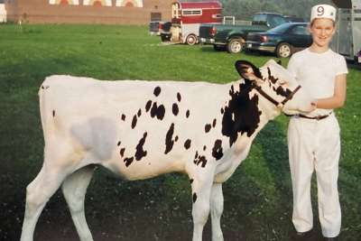 An archival photo of a young girl standing next to a cow