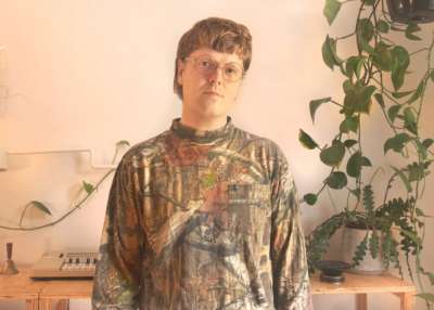 A young man in a cammo-print shirt standing in front of a turntable