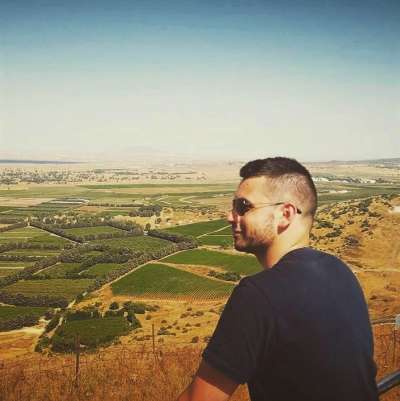 David Harary looks out from a hilltop over a hazy landscape with fields, bushes on desert, and a mountain in the distance.