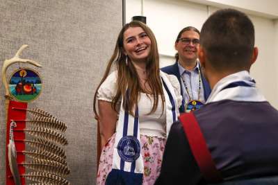 Alicia Corbiere, smiling, standing next to Indigenous symbols