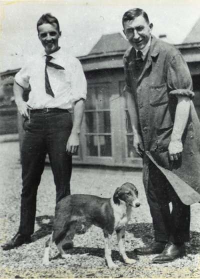 Charles Best and Frederick Banting smiles as they bend to pet a diabetic dog.