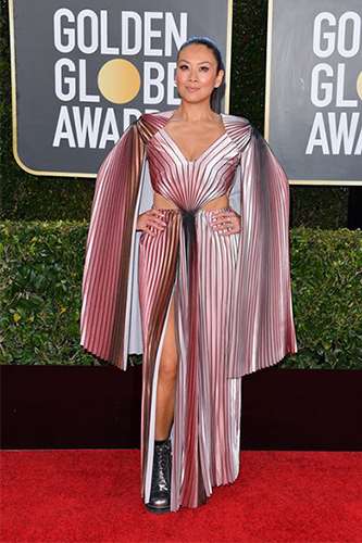 Lainey Lui smiles as she poses on the red carpet in an ombre pleated v-neck dress with caped sleeves and a high slit.