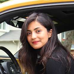 Sayeh Bayat smiling and sitting in the driver's seat of a car.