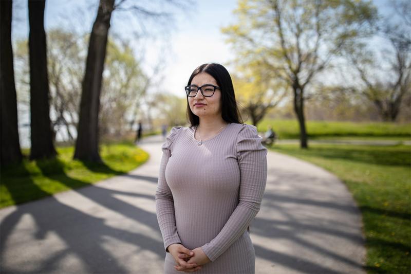 Khadija Hosseini stands on a wooded path by a lake.