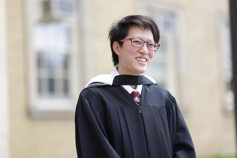 Alaina Luk smiles, wearing her graduation robes and hood.