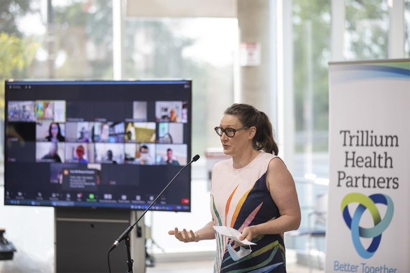 Alexandra Gillespie speaks at a microphone in front of a sign that reads: Trillium Health Partners better together.