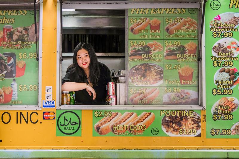 Joanna Luo smiles as she looks out the window of a food truck plastered with prices and images of burgers and fries.