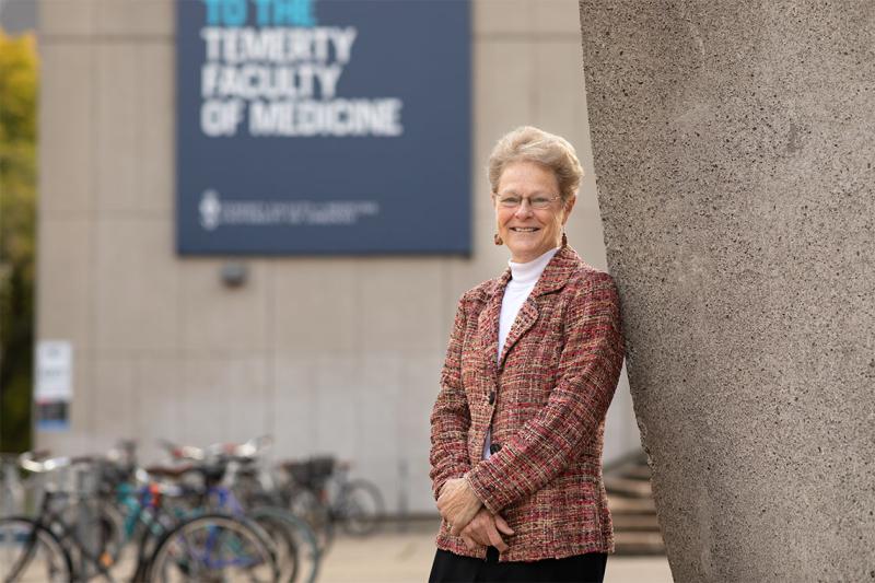 Patricia Brubaker smiles as she leans on the sculpture in front of the Medical Sciences Building at U of T.