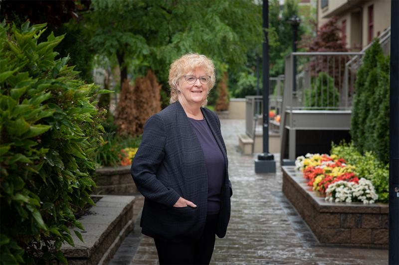 Ellen Hodnett smiles as she stands on a cobbled alleyway lined with gardens.