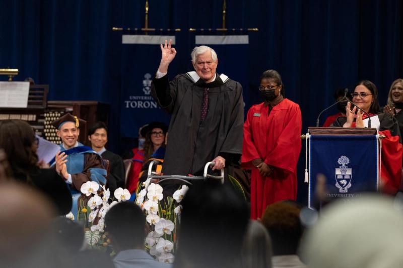 John Bond on the stage at graduation, making an OK sign with his hand