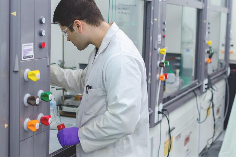 Wearing glasses and gloves, Aaron Cabal reaches into protectively walled lab bench that contains chemistry equipment.