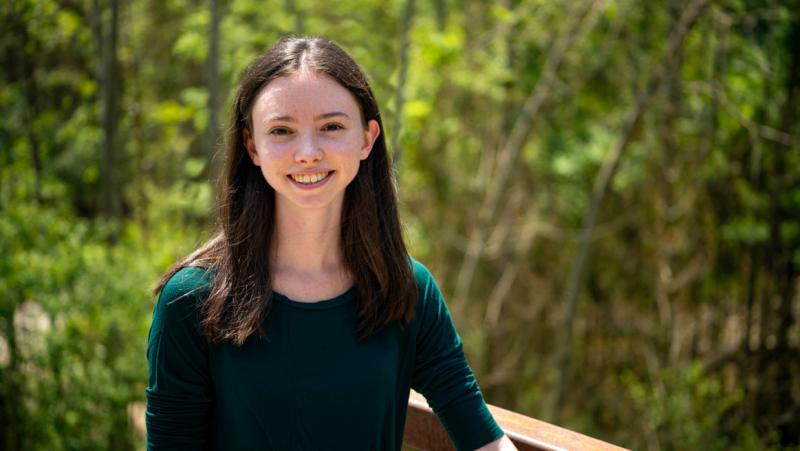Abigail Clapperton smiles while standing on a boardwalk in a forest.