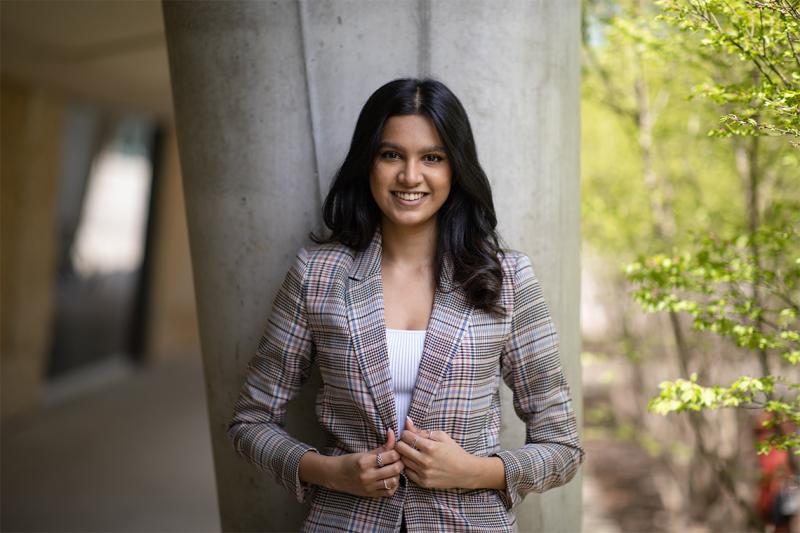 Aishwarya Nair smiles as she stands under the portico of a concrete building, next to a garden.