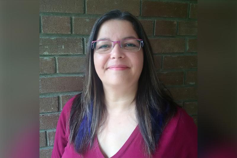 Angela Mashford-Pringle smiles as she stands outdoors by a brick wall.