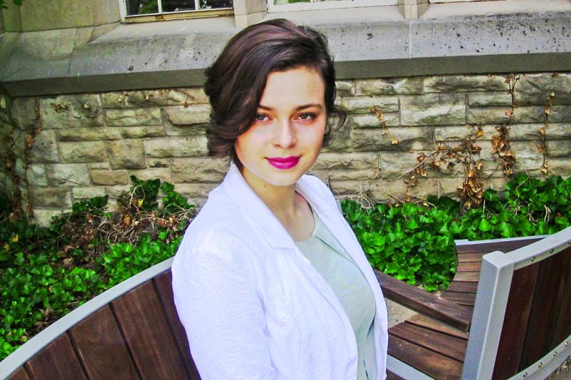 Anna Paliy smiles, sitting on a bench by an ivy-covered wall.
