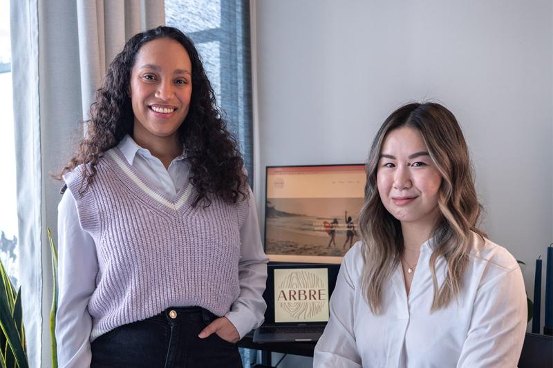 Kristina Knox and Stephanie Tien with a laptop showing a beach scene. A plaque that says Arbre sits on the keyboard.