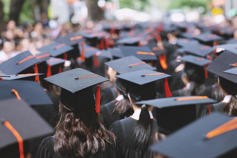 A crowd of students wearing graduation robes and mortarboard hats, seen from behind.