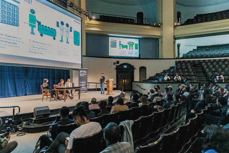 An audience in Convocation Hall watches a presentation on clean energy startup Reeddi.