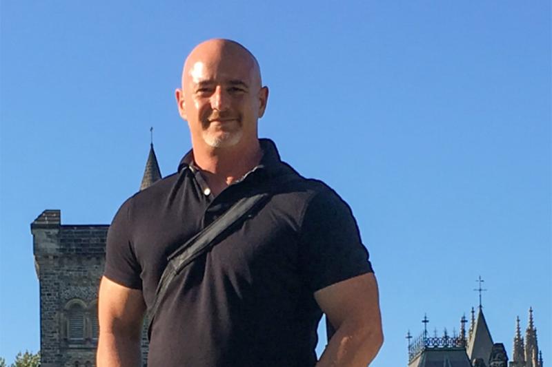 John Montefiore smiles, standing against a sunny sky on Front Campus.