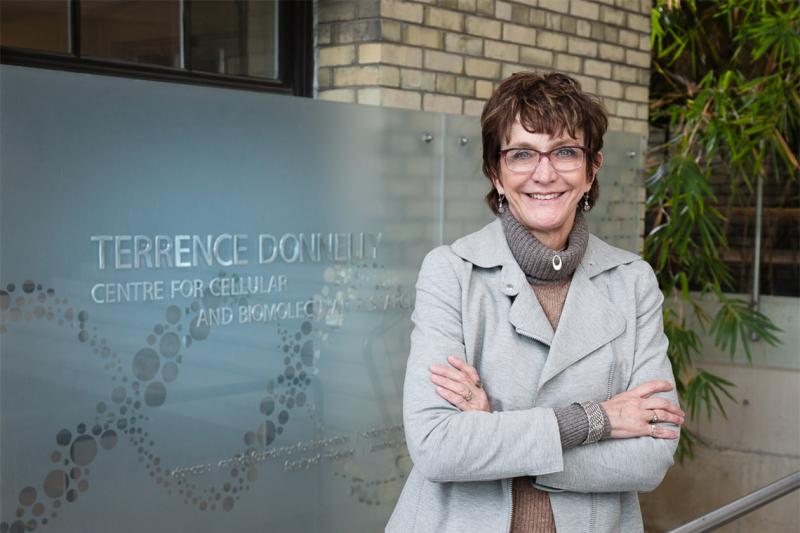 Brenda Andrews smiles as she stands beside a sign reading Terrence Donnelly Centre for Cellular and Biomolecular Research