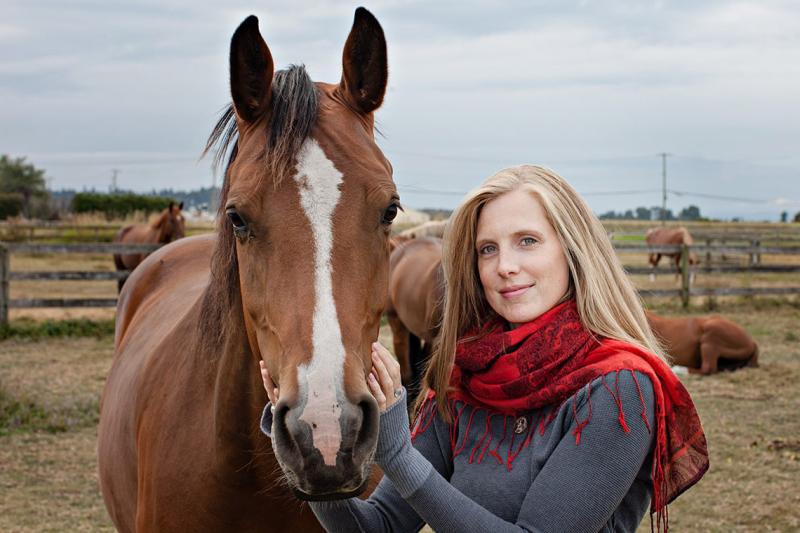 Carolyn Creed smiles as she pets a horse's face in an outdoor paddock.