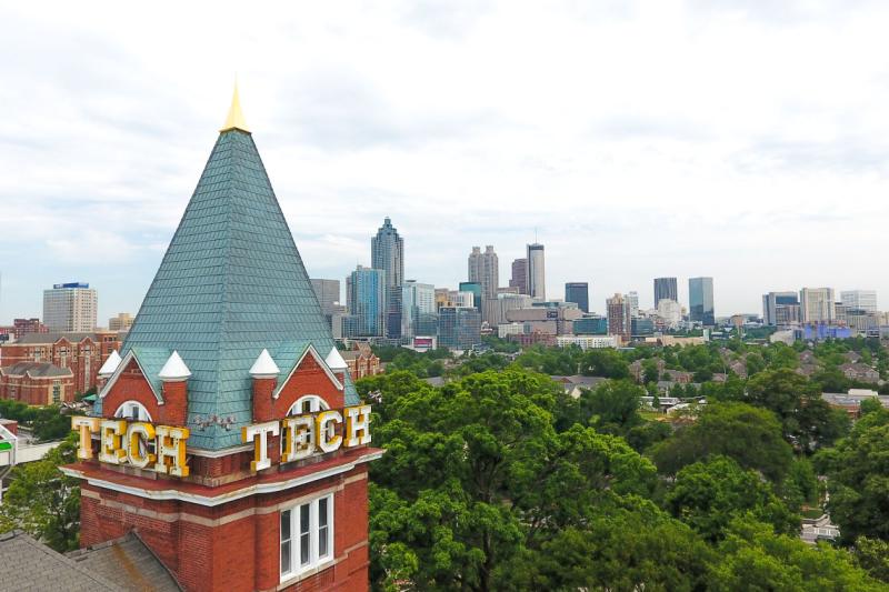The word TECH is blazoned on the roof of a tower overlooking a forested city campus.