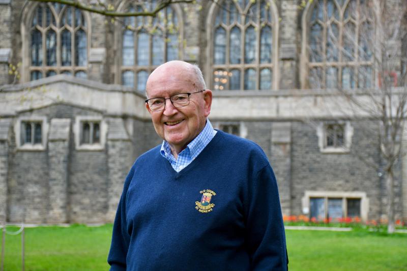 Bob Burrows in a blue sweater standing in front of Burwash Hall