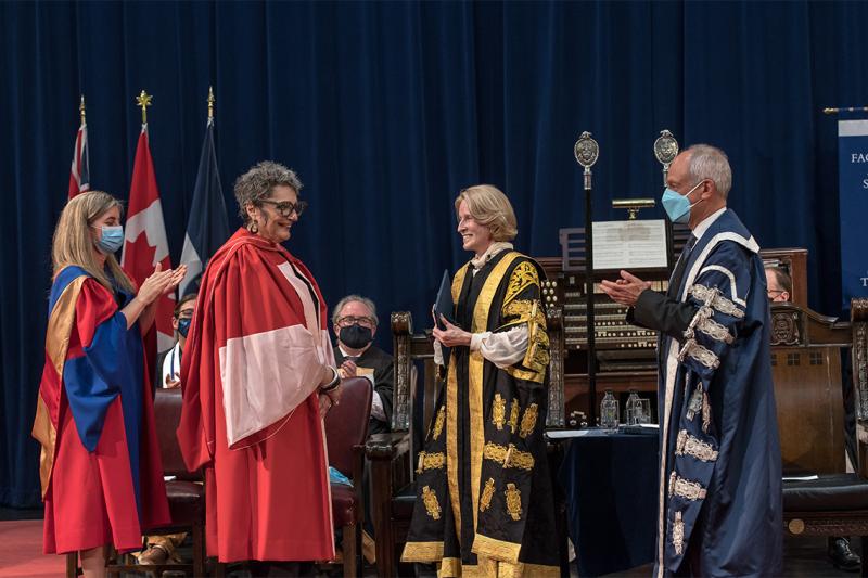 Nada Ristich smiles at Meric Gertler and Rose Patten, while a student puts on Nada's academic hood.