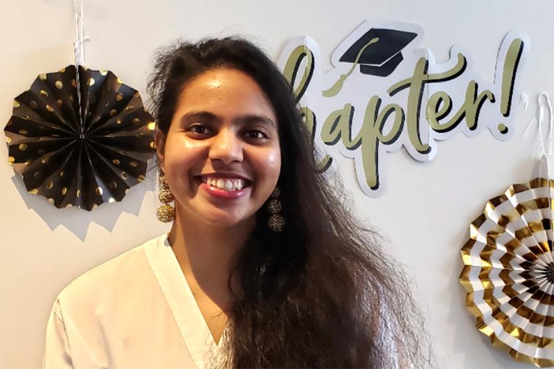 Dariya Darvin smiles as she stands in front of a backdrop with symbols of graduation such as an academic hat.