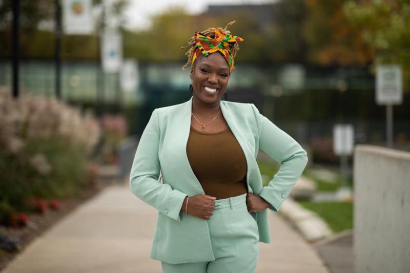 Desiree Kaunda-Wint smiles, standing with hand on hip on a walkway outdoors.