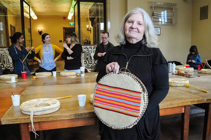 Elder Constance Simmonds smiles as she holds a flat drum top decorated with embroidery and still being stitched on the edges.