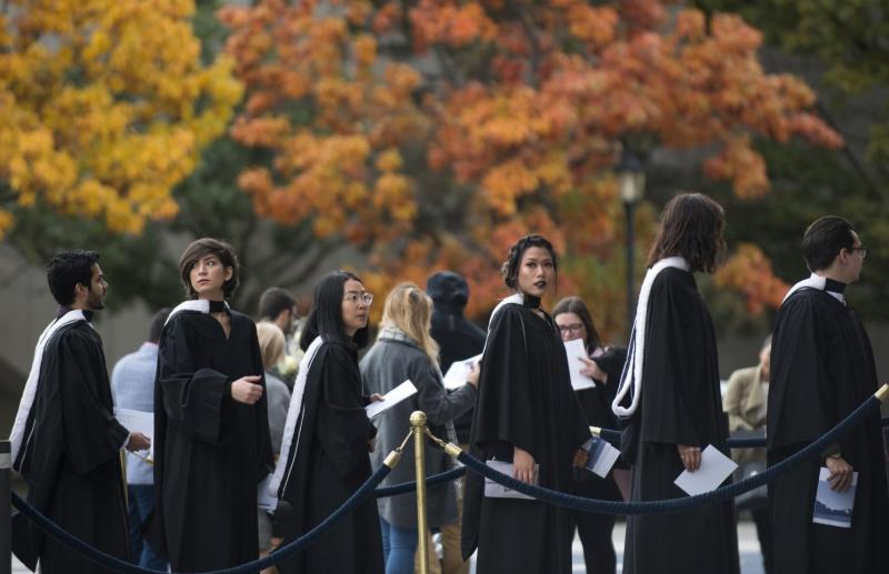 Graduates line up outside Convocation Hall in front of the fall foliage