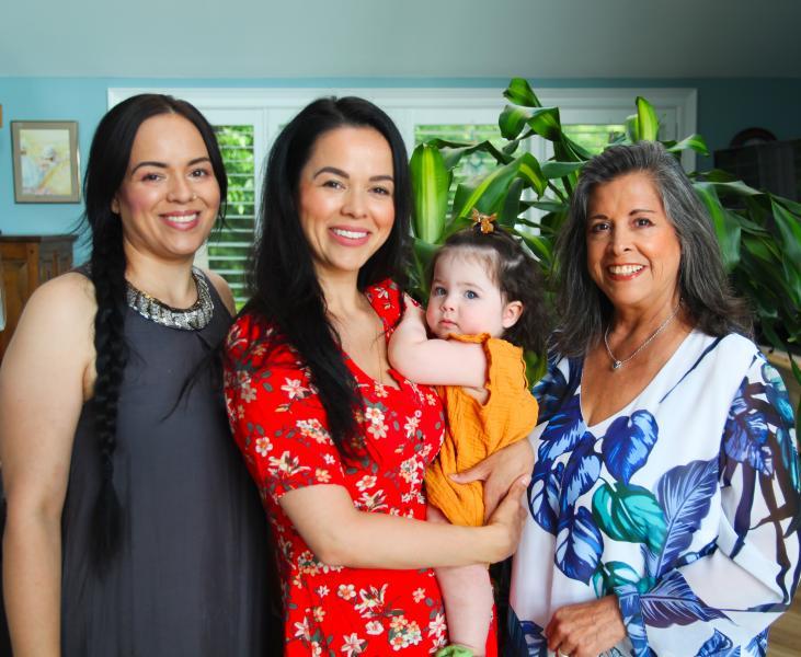 Cynthia Wesley-Esquimaux smiles as she stands next to her two daughters, one holding her own small daughter.