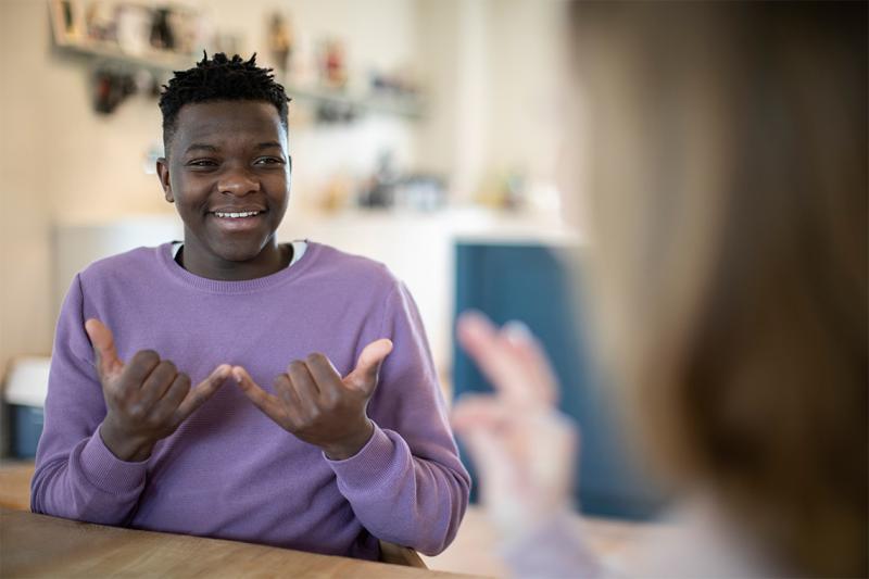 A young boy makes a Sign Language sign that means now, or today. 2 hands palms up, middle three fingers touching palms.
