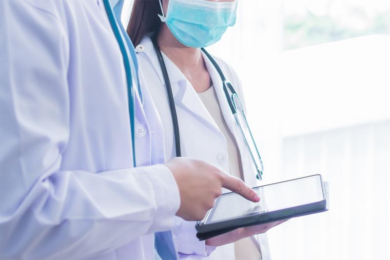 In a stock image, a man and a woman in white doctor's coats look at a tablet together.