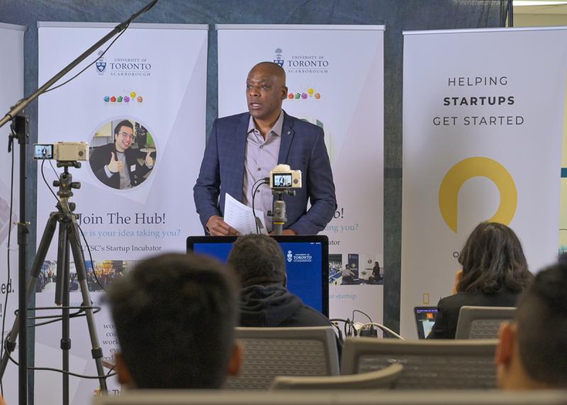 Donovan Dill speaks at a podium in front of banners. Text reads: Join the hub, helping startups get started.