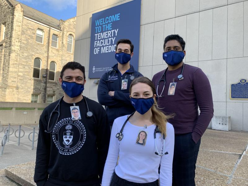 Damoon Ghahari, James Sanayei, Caroline Gregory and Rayoun Ramendra wear masks and laminated photos of themselves smiling.