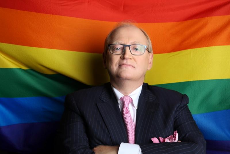 Douglas Elliott standing in front of a Pride flag
