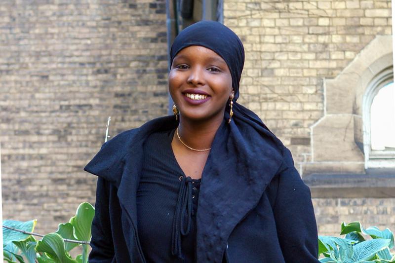 Ikran Jama smiles while standing in a garden outside a stone building.
