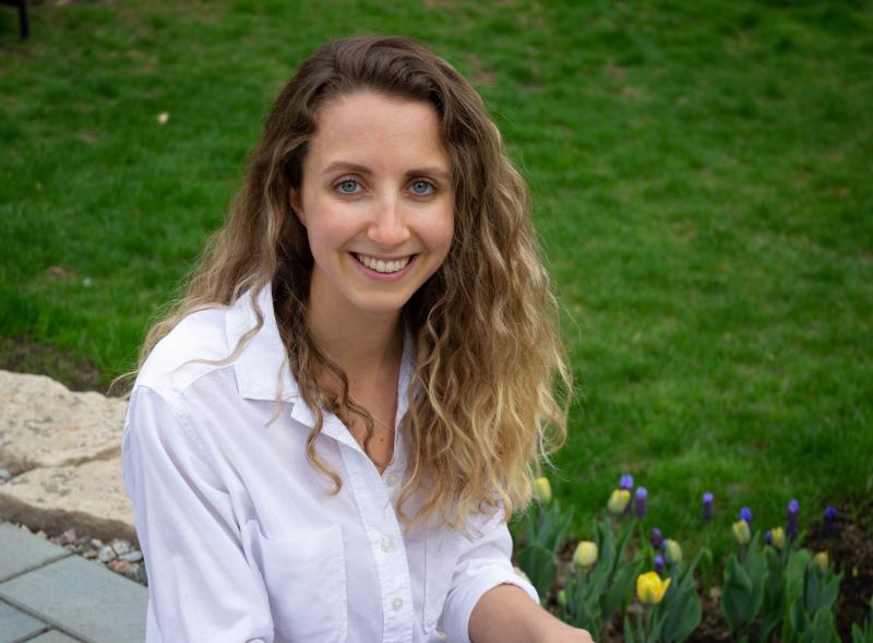 Jillian Sprenger smiles as she sits in a garden with blossoming tulips.